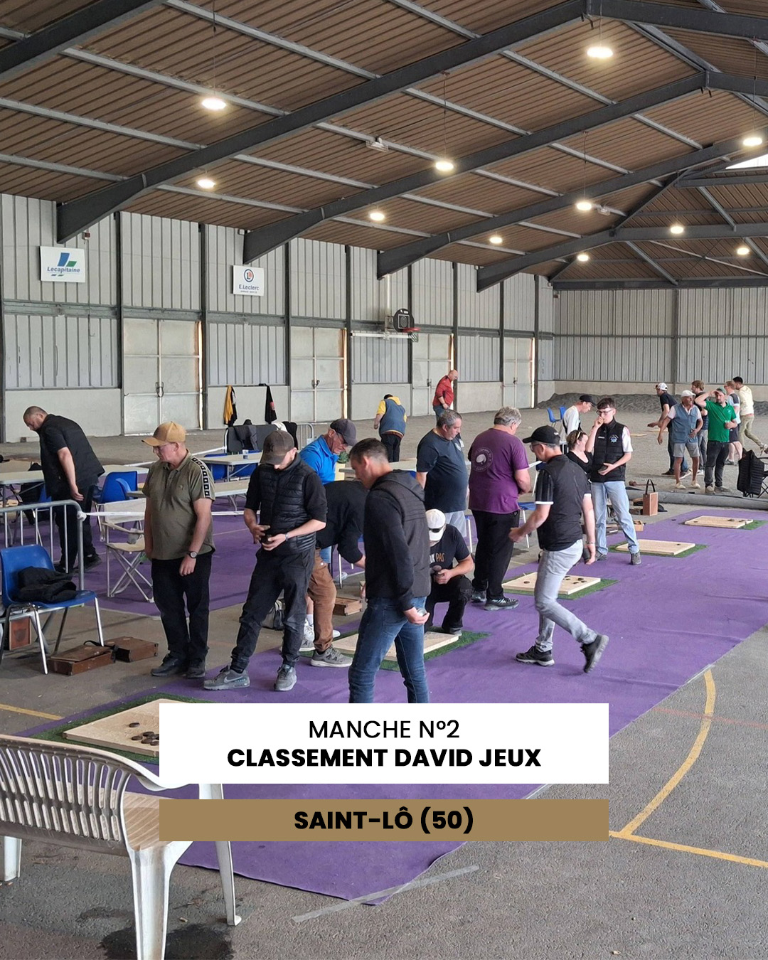 Indoor pétanque competition with players lining up on purple lanes; banner reads 'MANCHE N°2 CLASSEMENT DAVID JEUX SAINT-LÔ (50)'.