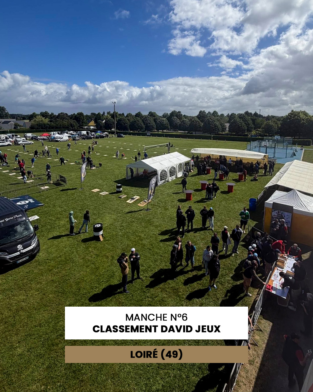 Outdoor community event on a grassy field with white tents, people mingling near booths, and a blue sky with clouds.
