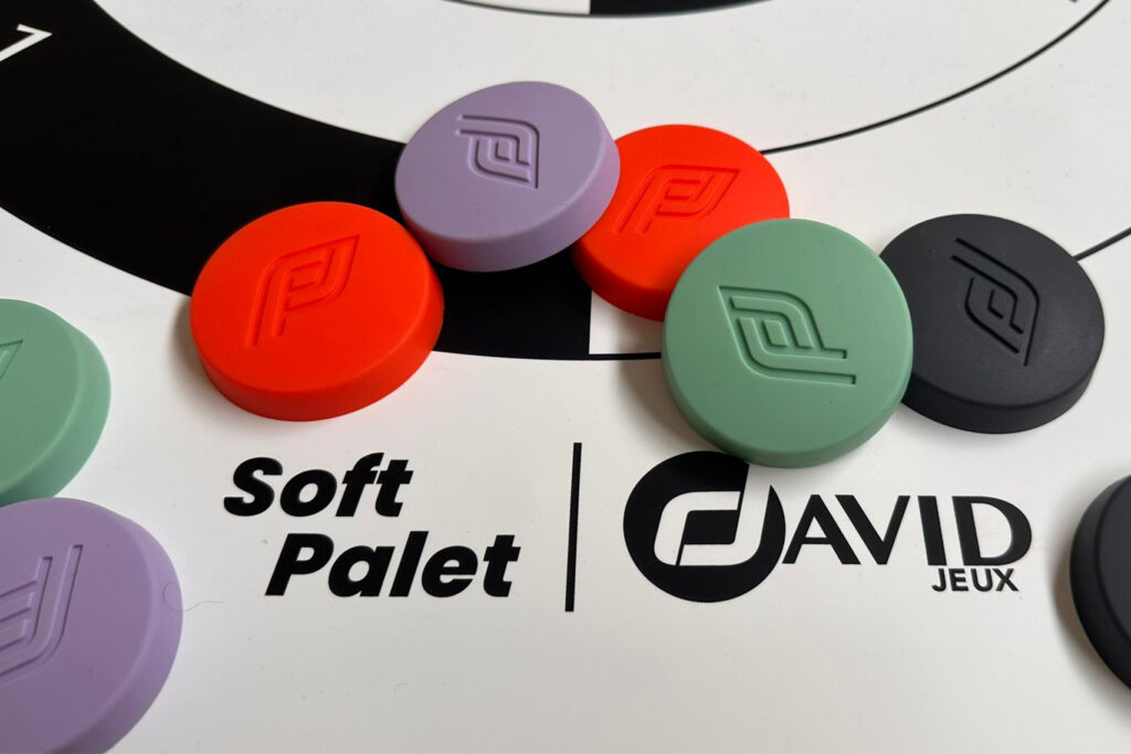 Colorful round game tokens with an embossed logo resting on a white surface beneath the text 'Soft Palet' and 'David Jeux'.