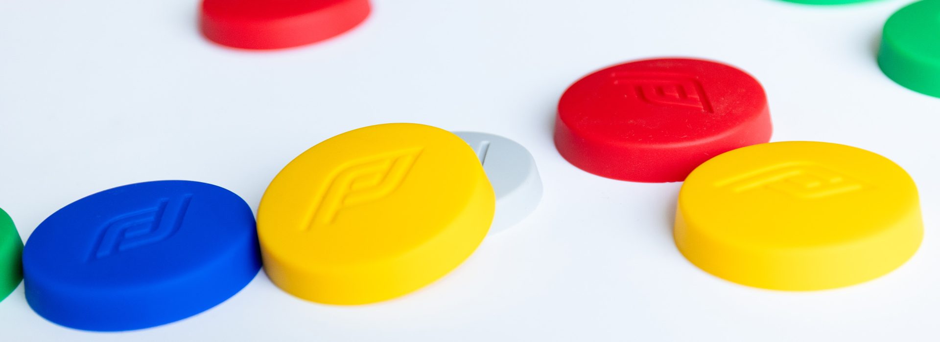 Assorted colorful plastic game pogs scattered on a white surface (blue, yellow, red, green).